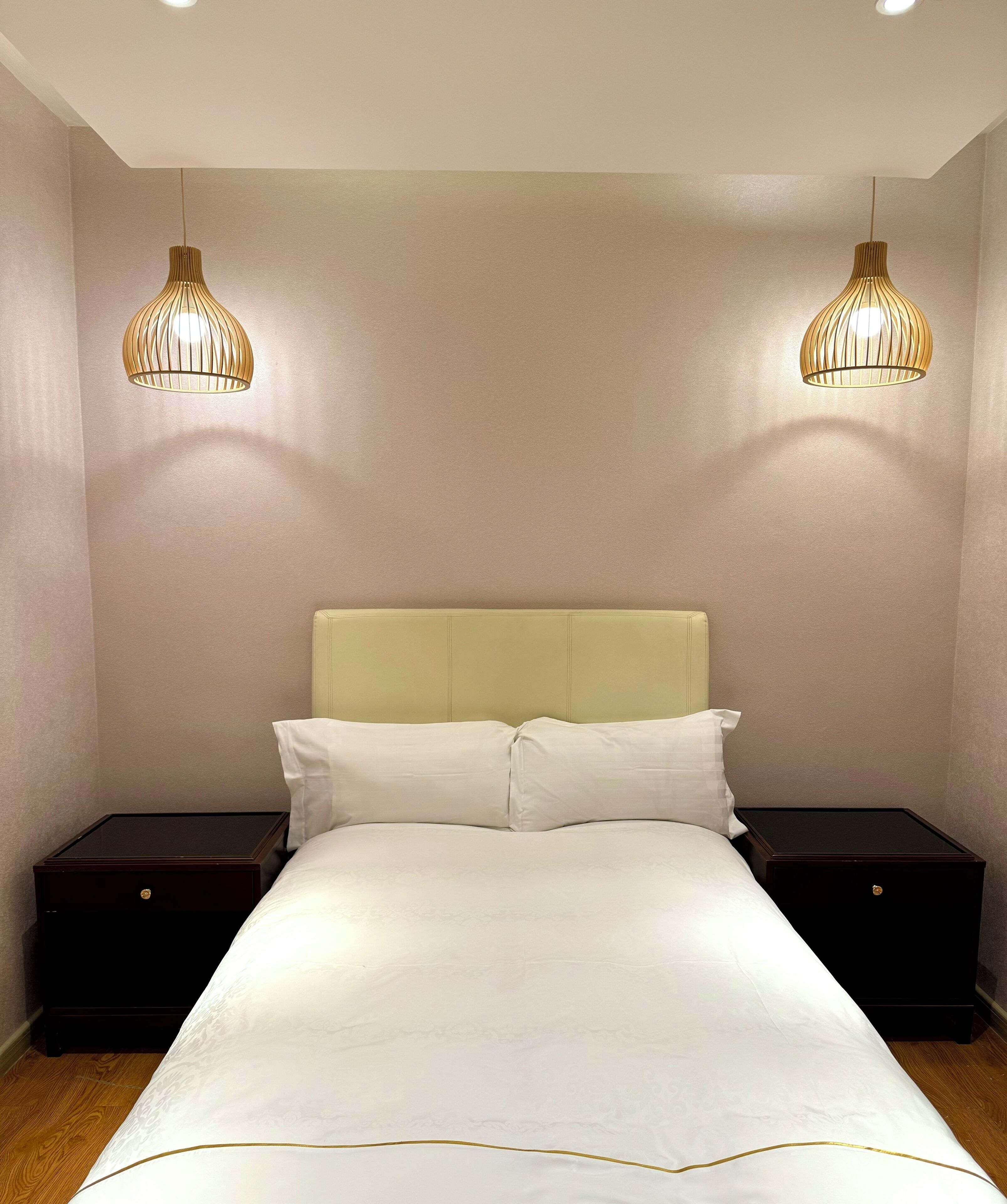 Una cama bien hecha con cabecera, dos mesitas de noche y dos lámparas colgantes.