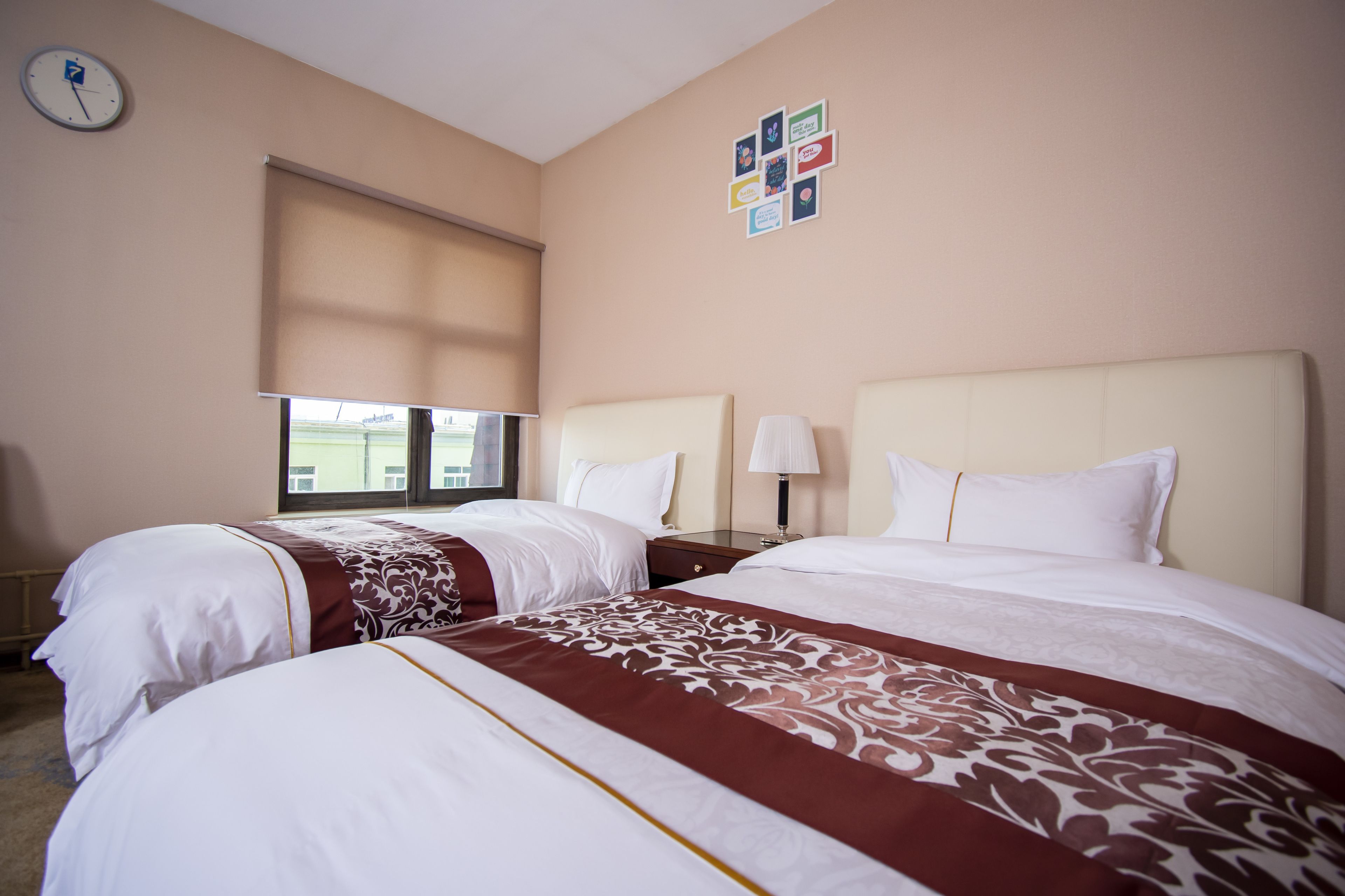 A hotel room with two beds, a clock on the wall, and a window with blinds.