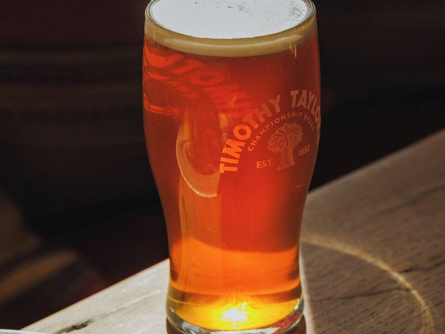 A glass of beer on a wooden table with a napkin and a plate of food.