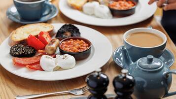 Una colazione servita con piatti di cibo, tazze di caffè e un teiera.