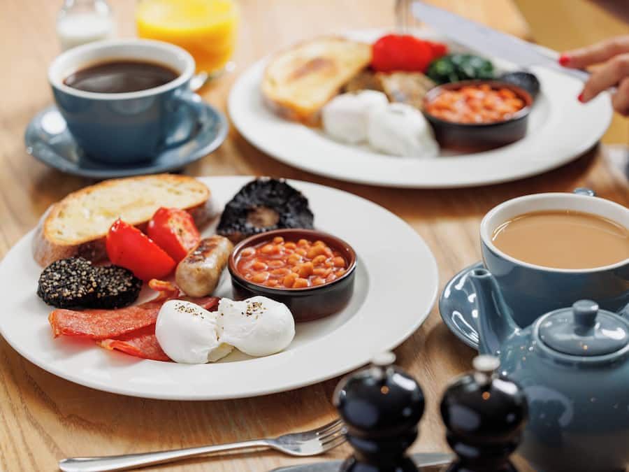 Una colazione servita con piatti di cibo, tazze di caffè e un teiera.
