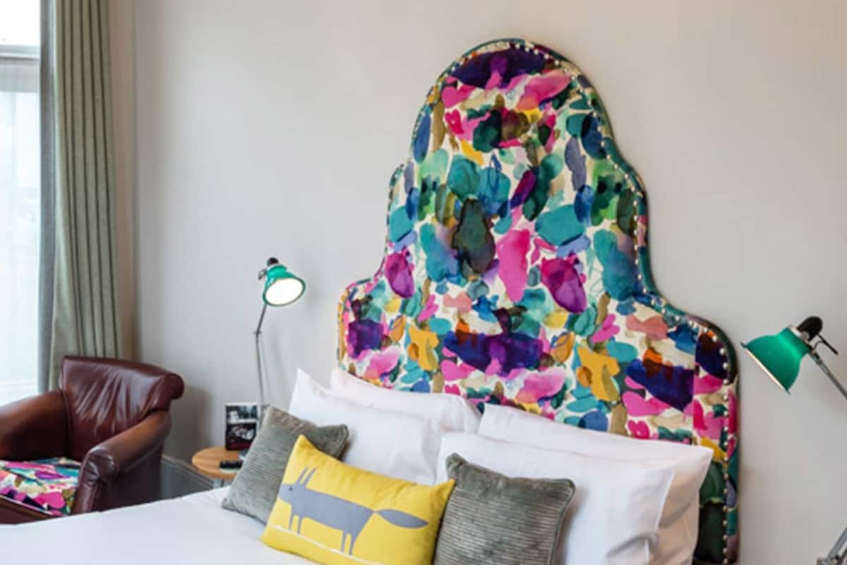 A bedroom with a bed, a chandelier, a chair, and a lamp.
