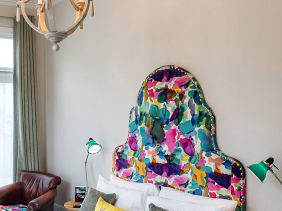 A bedroom with a bed, a chandelier, a chair, and a lamp.