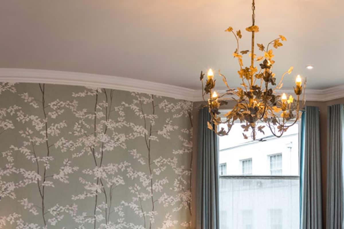 A bedroom with a large bed, a chandelier, a chair, and a view of the city through the window.