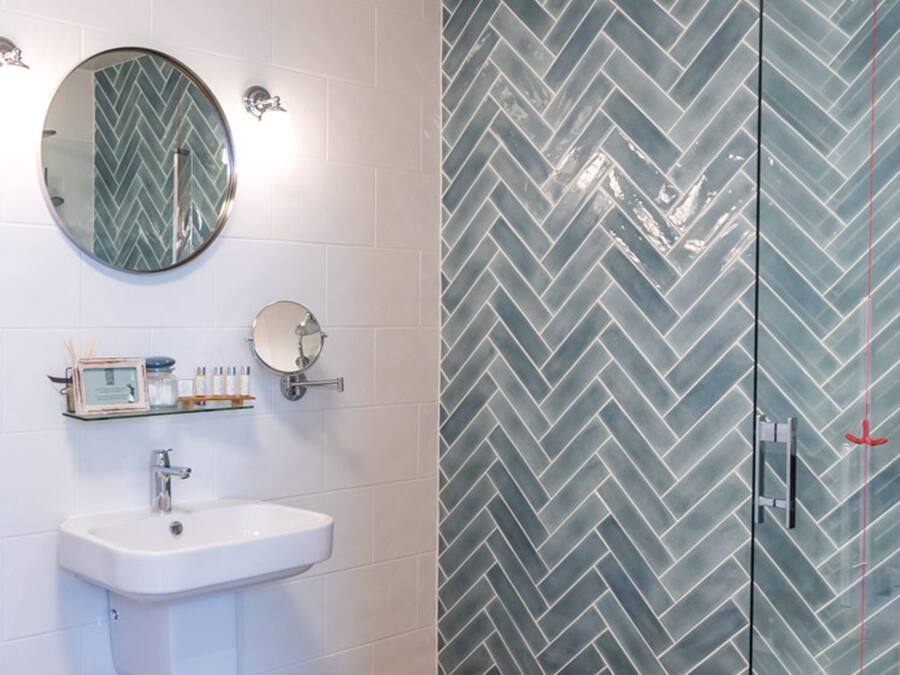 A bathroom with a white sink, mirror, and herringbone-patterned tiles.