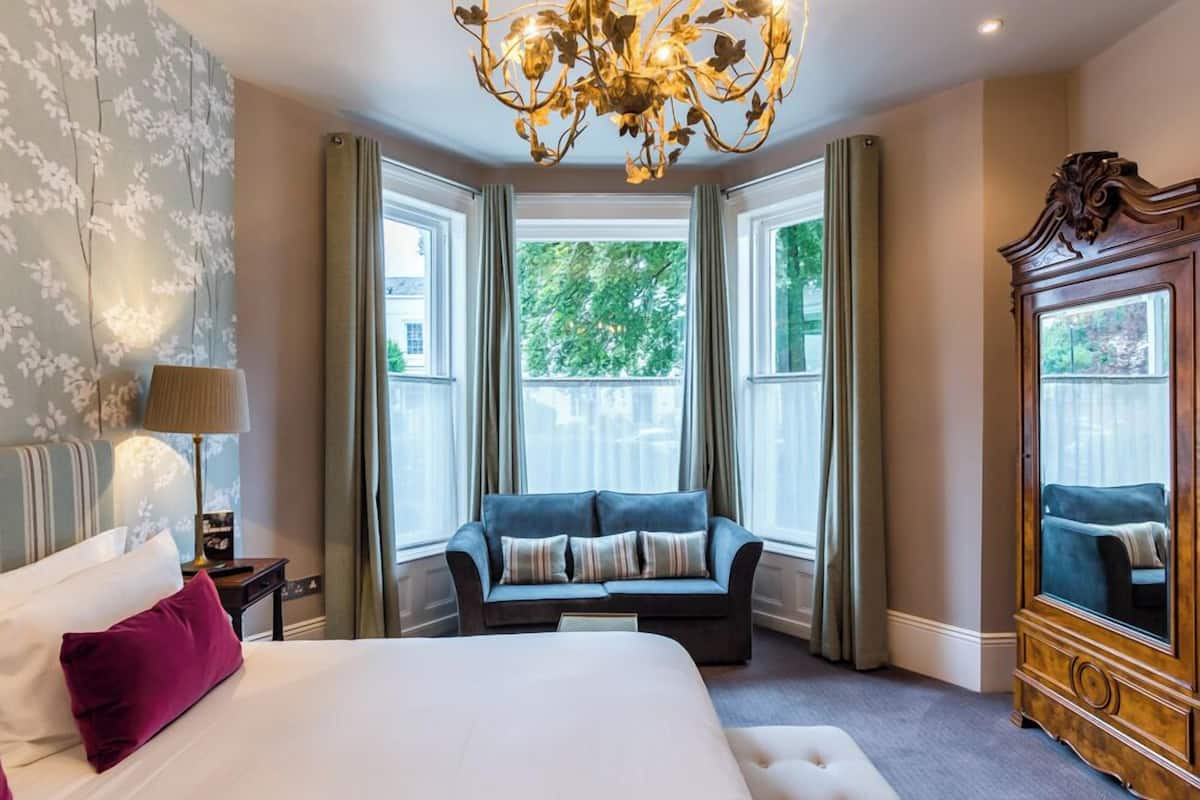 A hotel room with a large bed, a sofa, a chandelier, and a large mirror.