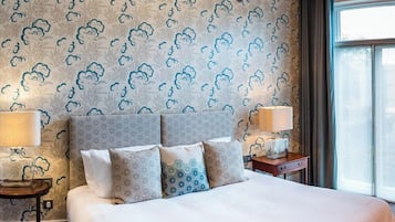 Ein Hotelzimmer mit einem großen Bett, zwei Nachttischen mit Lampen, einer Chandelüster und einem Fenster mit Vorhängen.