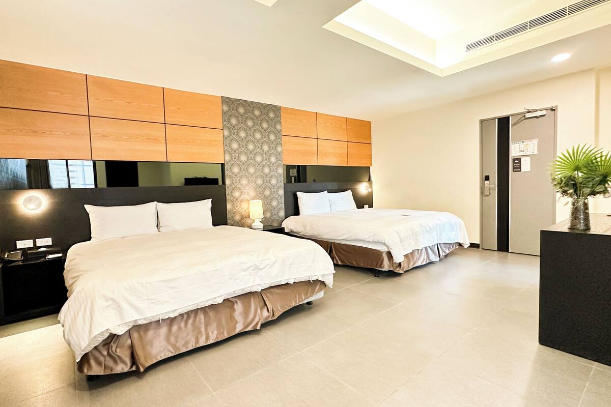 A hotel room with two beds, a desk, a mirror, and a plant.