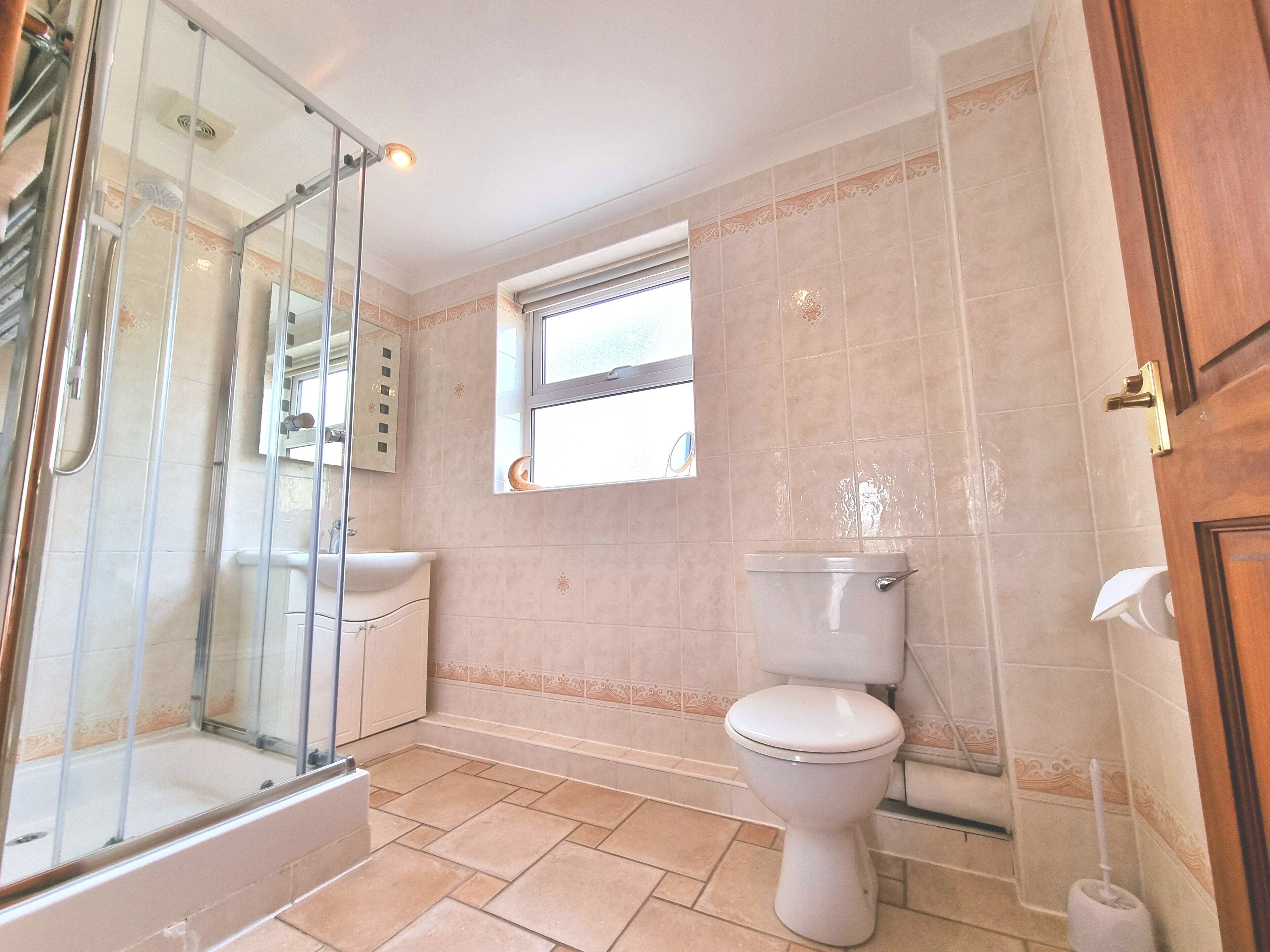 A bathroom with a glass shower enclosure, a toilet, and a window.