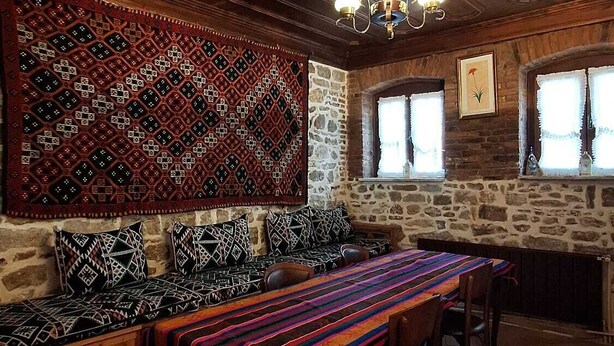 A cozy room with a wooden ceiling, stone walls, a patterned rug, and a bench with cushions. - Mihran Hanım Konagi (Edirne)