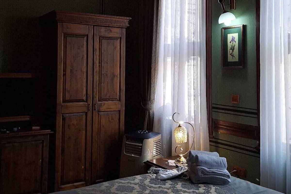 A dimly lit room with a bed, a wooden wardrobe, a radiator, and a chandelier.