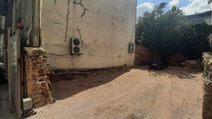A narrow alleyway with a dirt ground, a brick wall on one side, and a white building with a satellite dish on the other. - Mihran Hanım Konagi (Edirne)