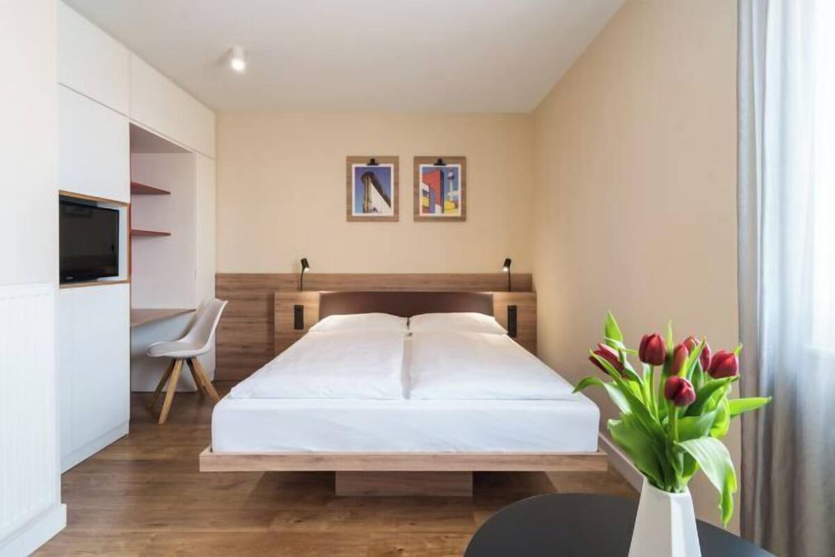 Un dormitorio con una cama, una silla, un televisor y dos cuadros en la pared.