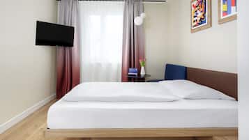 Habitación de hotel con cama, televisor de pantalla plana, una mesita con un florero y cuadros en la pared.