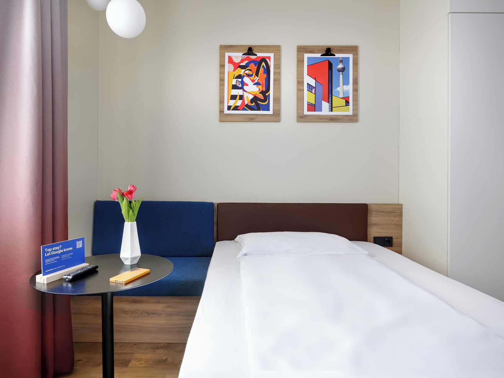 A hotel room with a bed, a blue sofa, a small table with a vase of flowers, and two framed artworks on the wall.