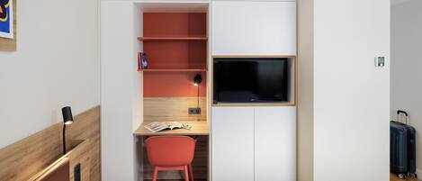 A hotel room with a bed, a desk with a chair, a TV, and a suitcase.