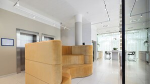 Eine moderne Lobby mit einer großzügigen, gebogenen Sitzgruppe, einem Empfangsbereich und einem sichtbaren Aufzug.