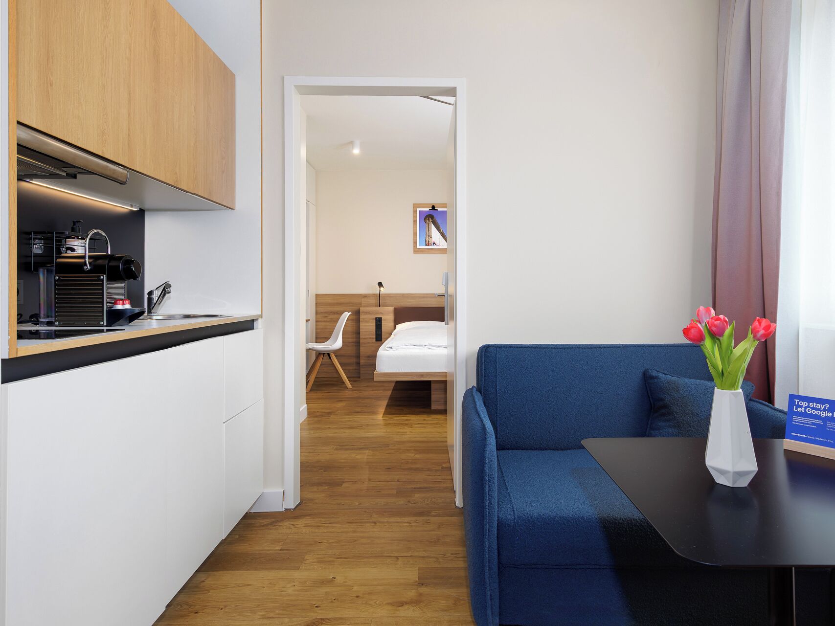 Ein Hotelzimmer mit Küchenzeile, einem blauen Sofa, einem kleinen Tisch und einer Vase mit Blumen.