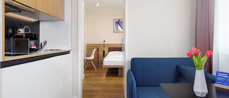 Una habitación de hotel con kitchenette, un sofá azul, una mesita y un florero con flores.