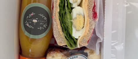 A sandwich with lettuce and eggs, a bottle of juice, and a packaged food item in a box.