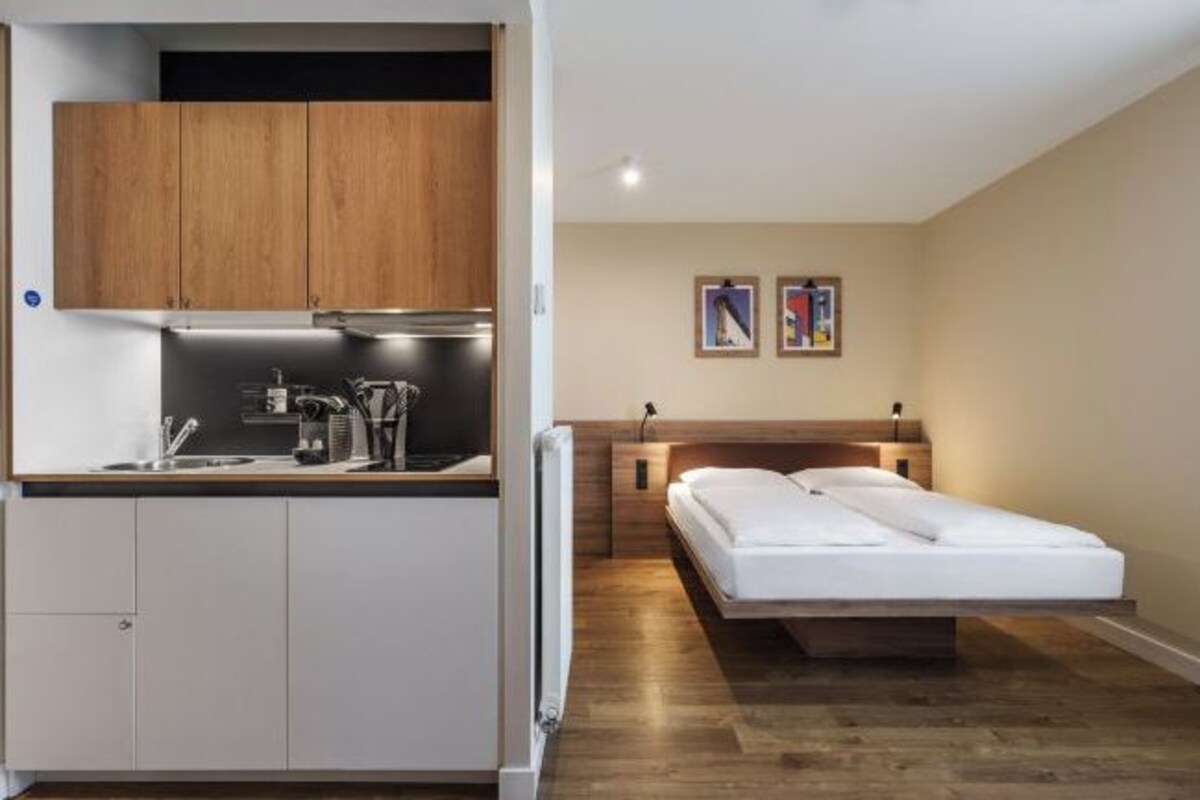 Een compacte kamer met een kitchenette, een bed en twee ingelijste foto's aan de muur.
