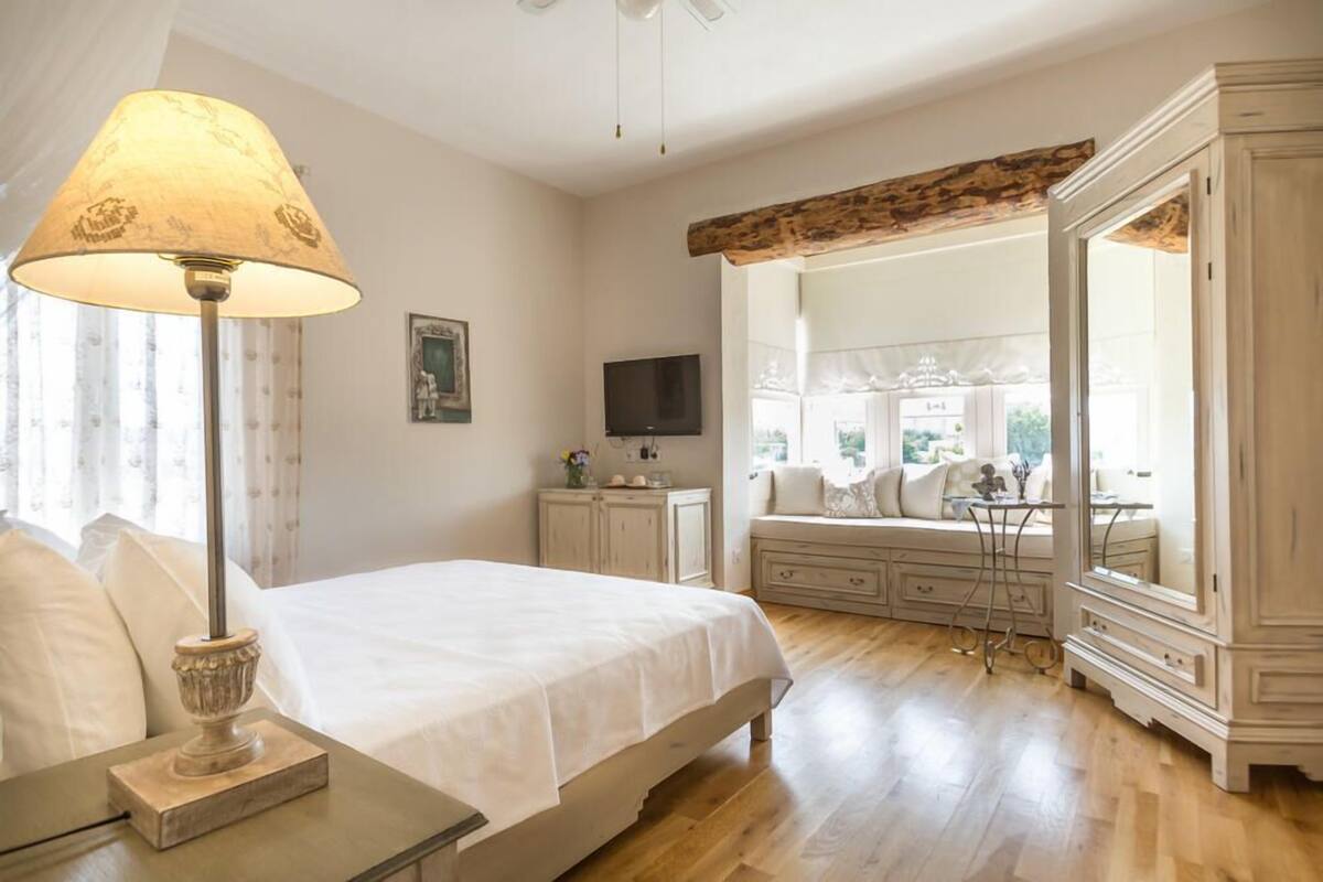 A bedroom with a bed, a bedside lamp, a TV, a dresser, and a large mirror.