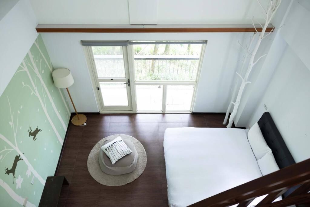 A bedroom with a bed, a window, a lamp, and a wall with a tree decal.