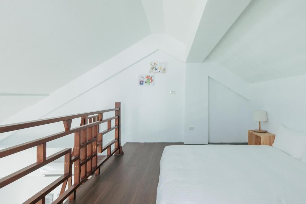 A bedroom with a wooden bed, a nightstand, a lamp, and a white wall with two small pictures.