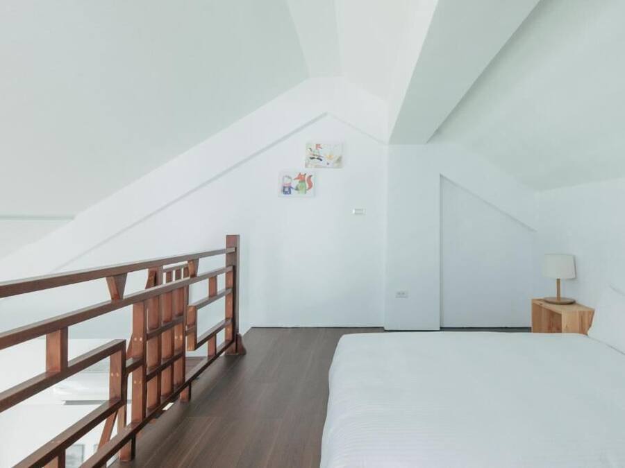 A bedroom with a wooden bed, a nightstand, a lamp, and a white wall with two small pictures.