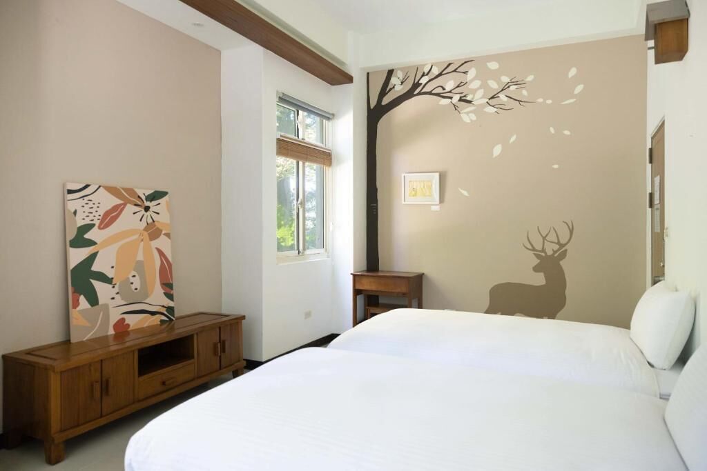 A bedroom with a large bed, a wooden cabinet, a window, and wall art including a deer silhouette and abstract painting.