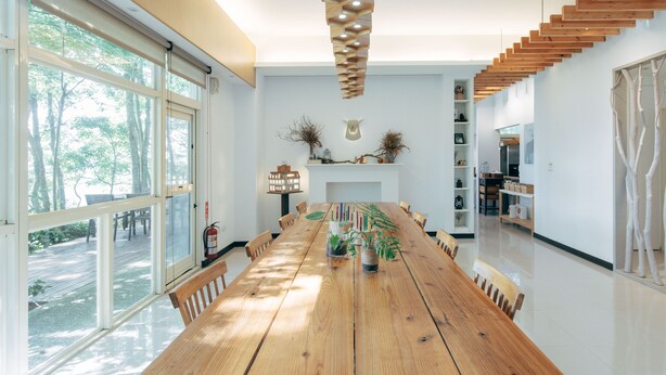A spacious dining area with a long wooden table, surrounded by chairs, and a staircase leading to an upper level. - Lvbolang by REINDEER, Sanyi (Sanyi)