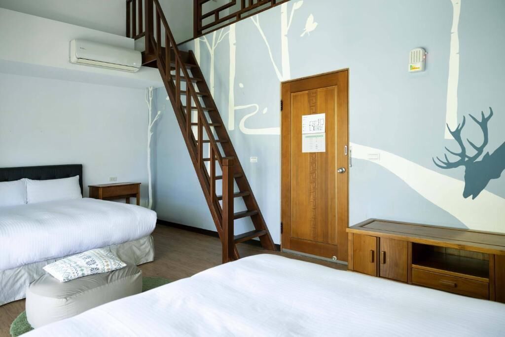 A bedroom with two beds, a wooden wardrobe, a small bedside table, and a wall mural.