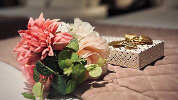 Una cama con un edredón rosa, una caja decorativa blanca con lazo dorado y un ramo de flores rosa y blanca.