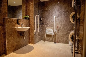Een moderne badkamer met een wastafel, spiegel en een douche toegankelijk voor rolstoelgebruikers.