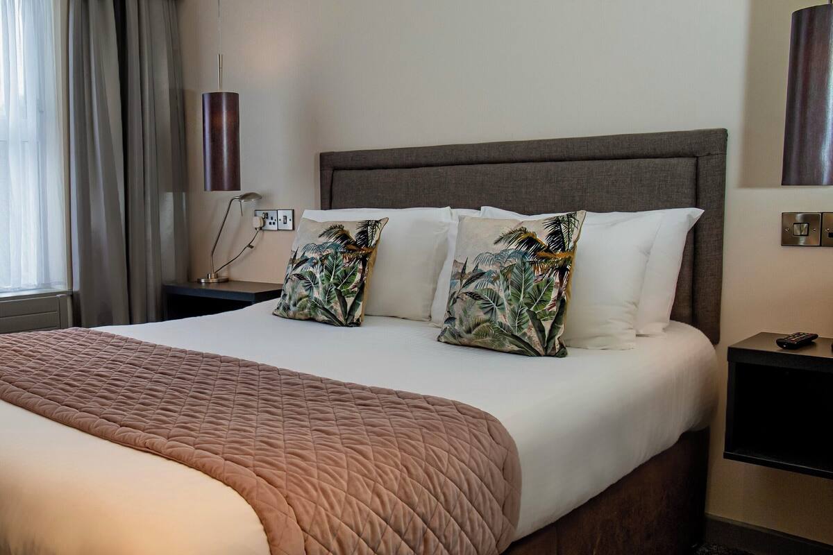 Una habitación de hotel con una cama grande, una mesita de noche, una lámpara y una lámpara de pared.