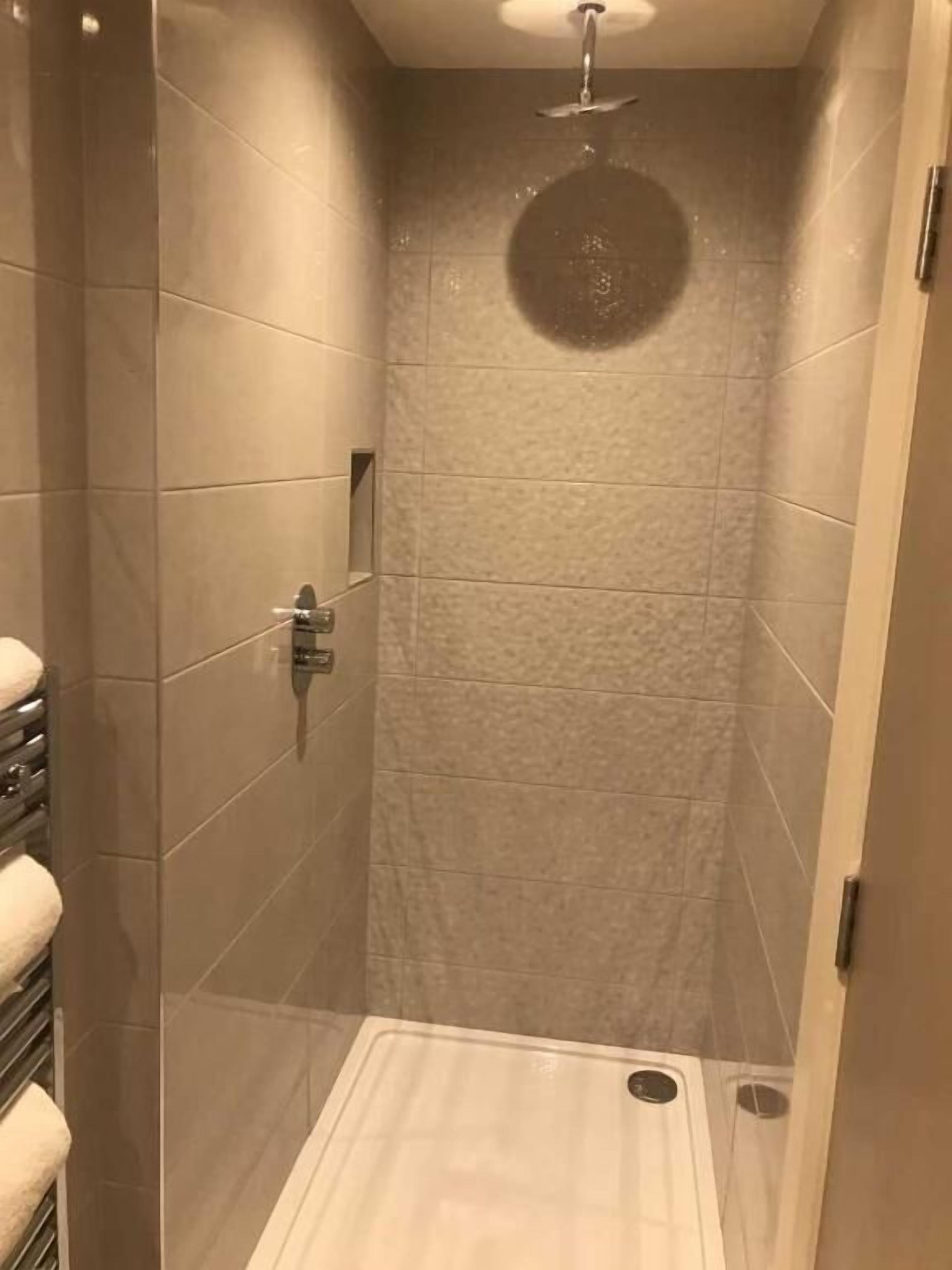 Una ducha a ras de suelo con puerta de cristal, paredes de azulejos y un cabezal de ducha.
