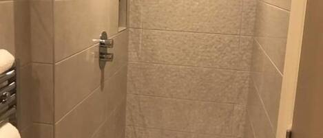 Una ducha a ras de suelo con puerta de cristal, paredes de azulejos y un cabezal de ducha.