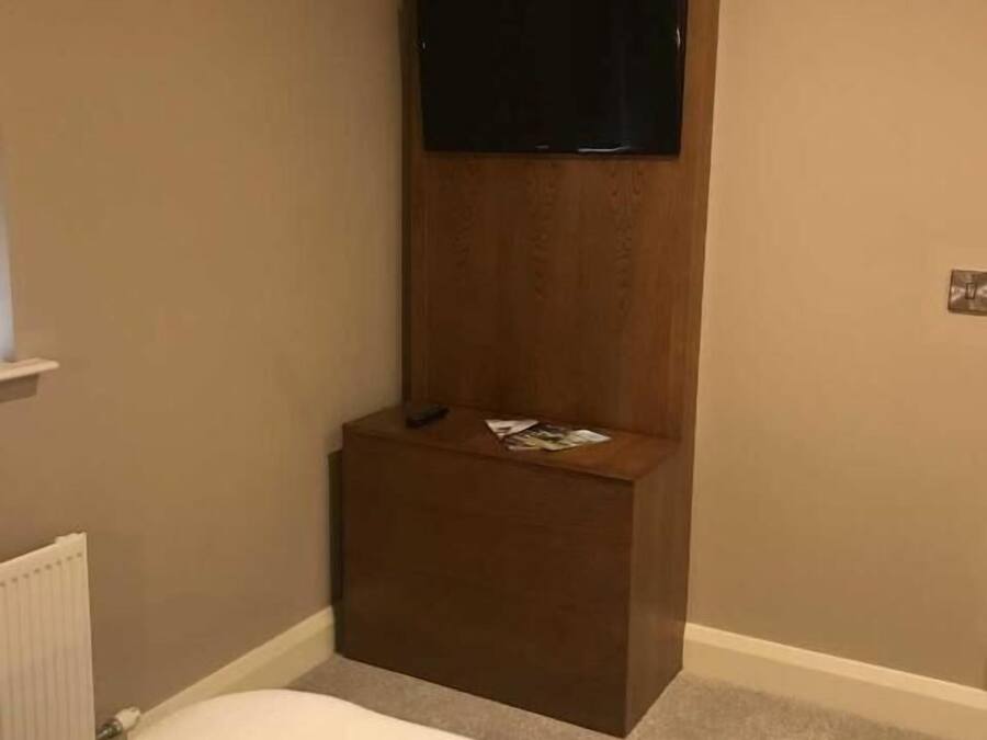 A hotel room with a bed, a small wooden side table, a flat-screen TV mounted on the wall, and a radiator.