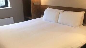 Una cama bien hecha con sábanas blancas en una habitación con cabecera de madera y estanterías empotradas.