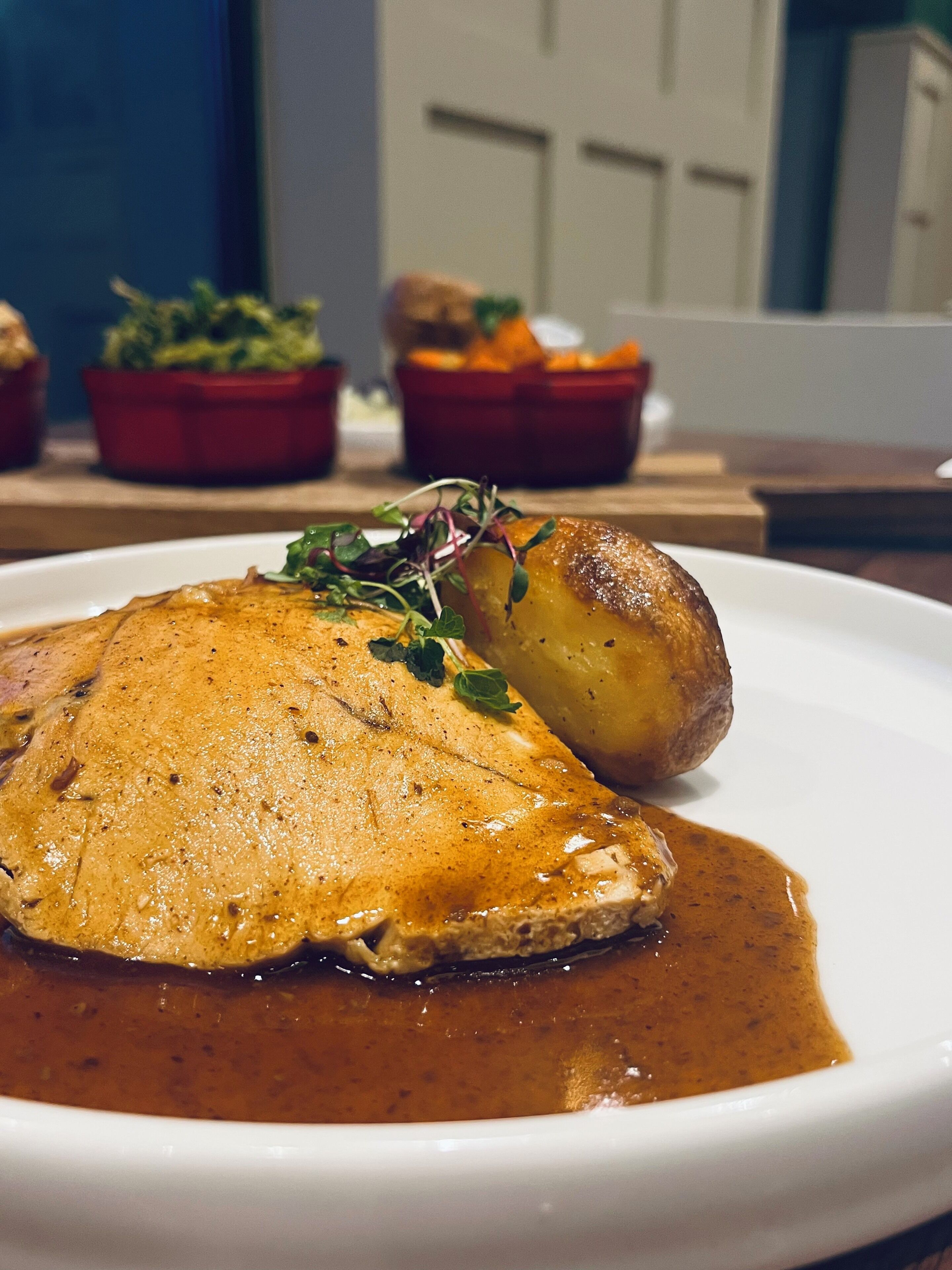 Un plato de pollo asado con salsa y una guarnición de papas al horno.