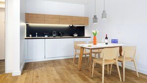 Una cocina moderna con armarios blancos, una encimera negra y sillas de madera alrededor de una mesa blanca.