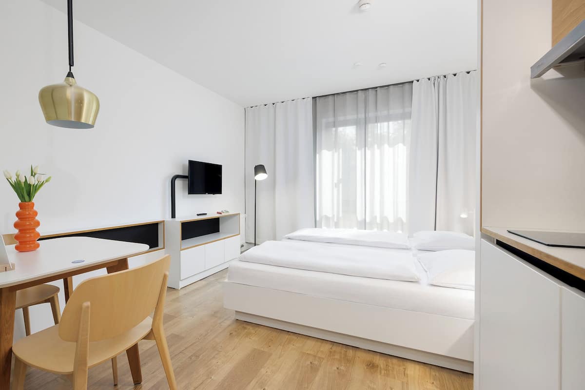 A modern hotel room with a bed, a desk, a chair, a TV, and a window with curtains.