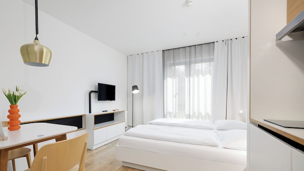 Una habitación de hotel moderna con una cama, un escritorio, una silla, un televisor y una ventana con cortinas.