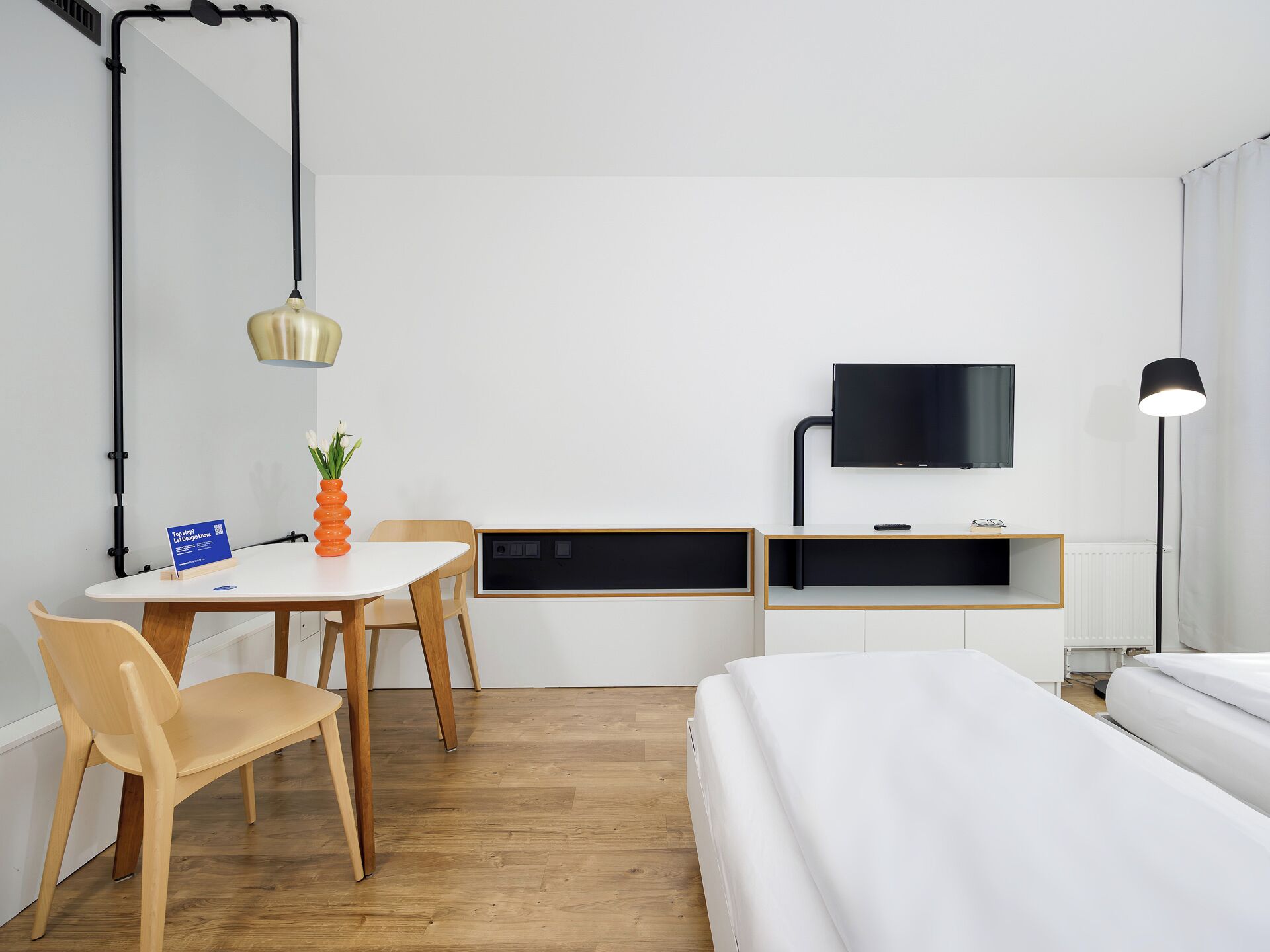 Habitación de hotel con cama, escritorio, silla, televisor y lámpara.