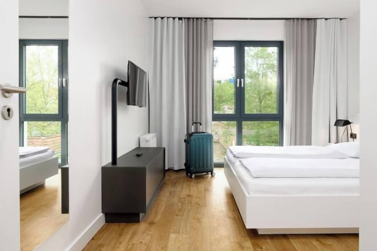 A modern hotel room with a bed, a desk, a television, and a suitcase.