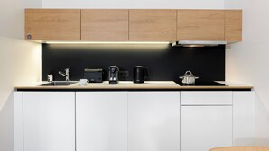 Una cocina moderna con salpicadero negro, armarios de madera, un lavamanos de acero inoxidable y una cafetera negra.