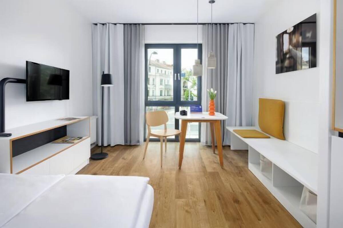 A hotel room with a bed, a desk, a chair, a table with a pineapple, and a TV mounted on the wall.
