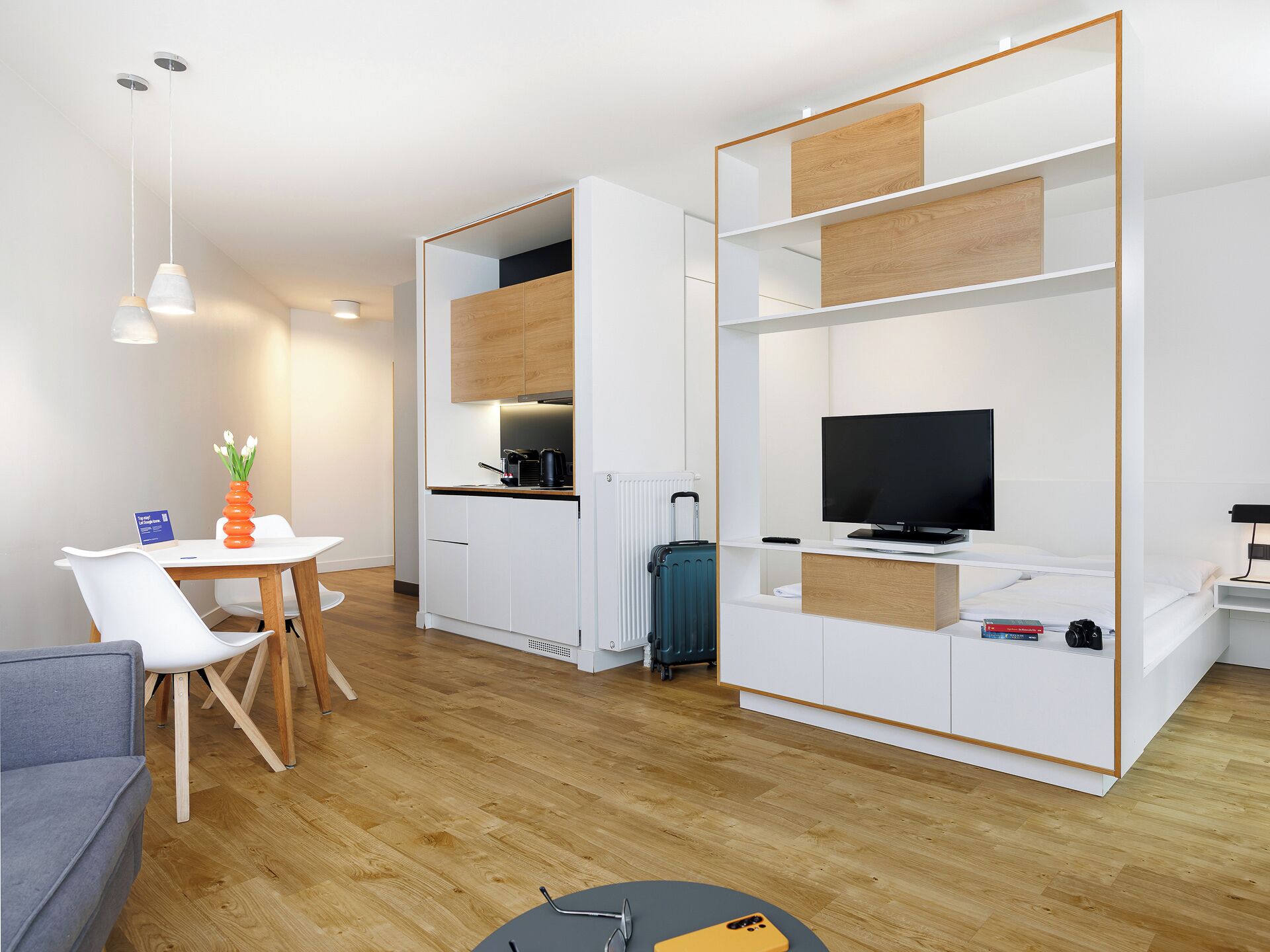 Une chambre d’hôtel moderne dotée d’une kitchenette, d’un téléviseur à écran plat, d’un canapé et d’un coin repas.