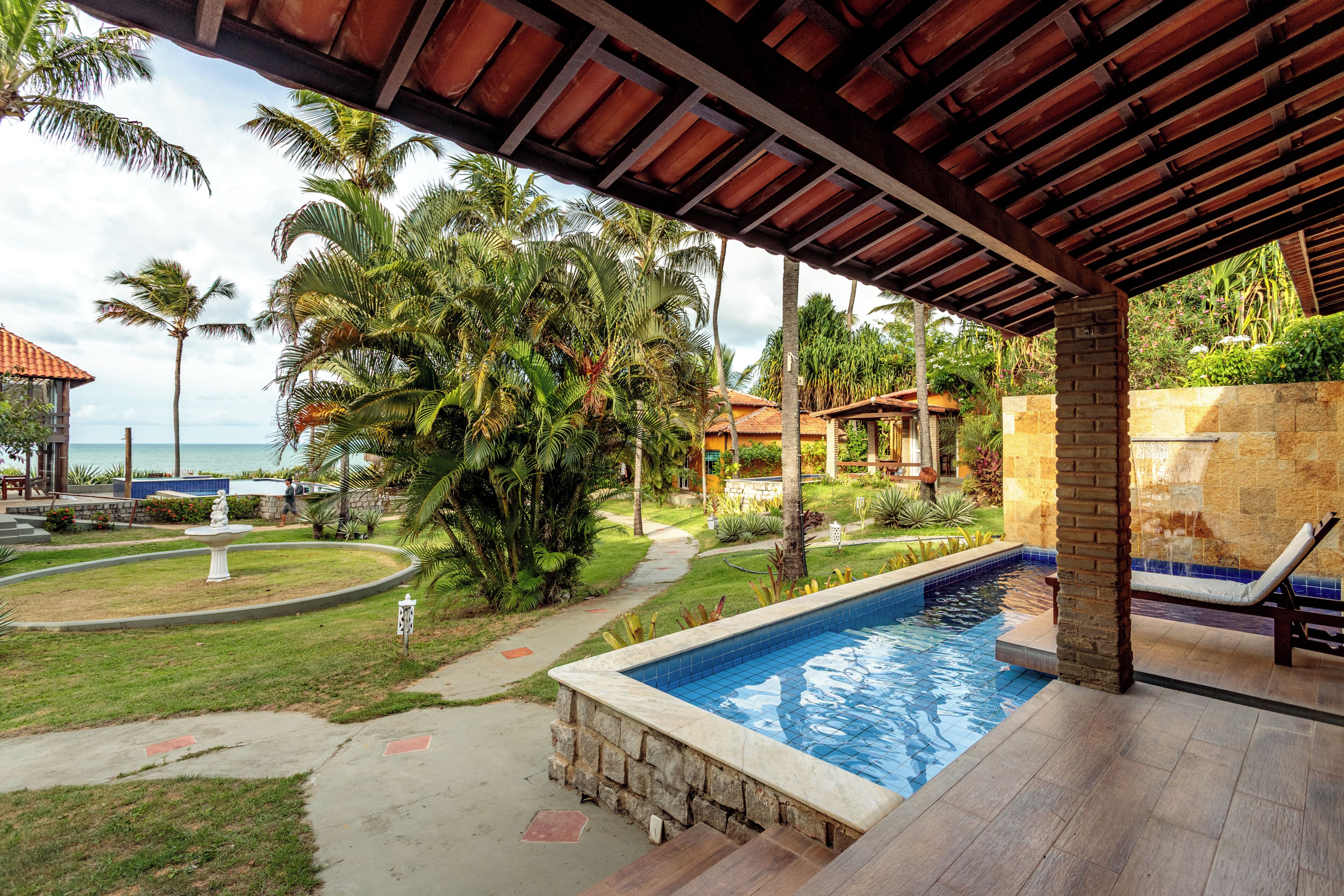 A pool area with a tiled deck, palm trees, and a view of the ocean.