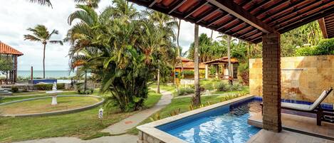 A pool area with a tiled deck, palm trees, and a view of the ocean.